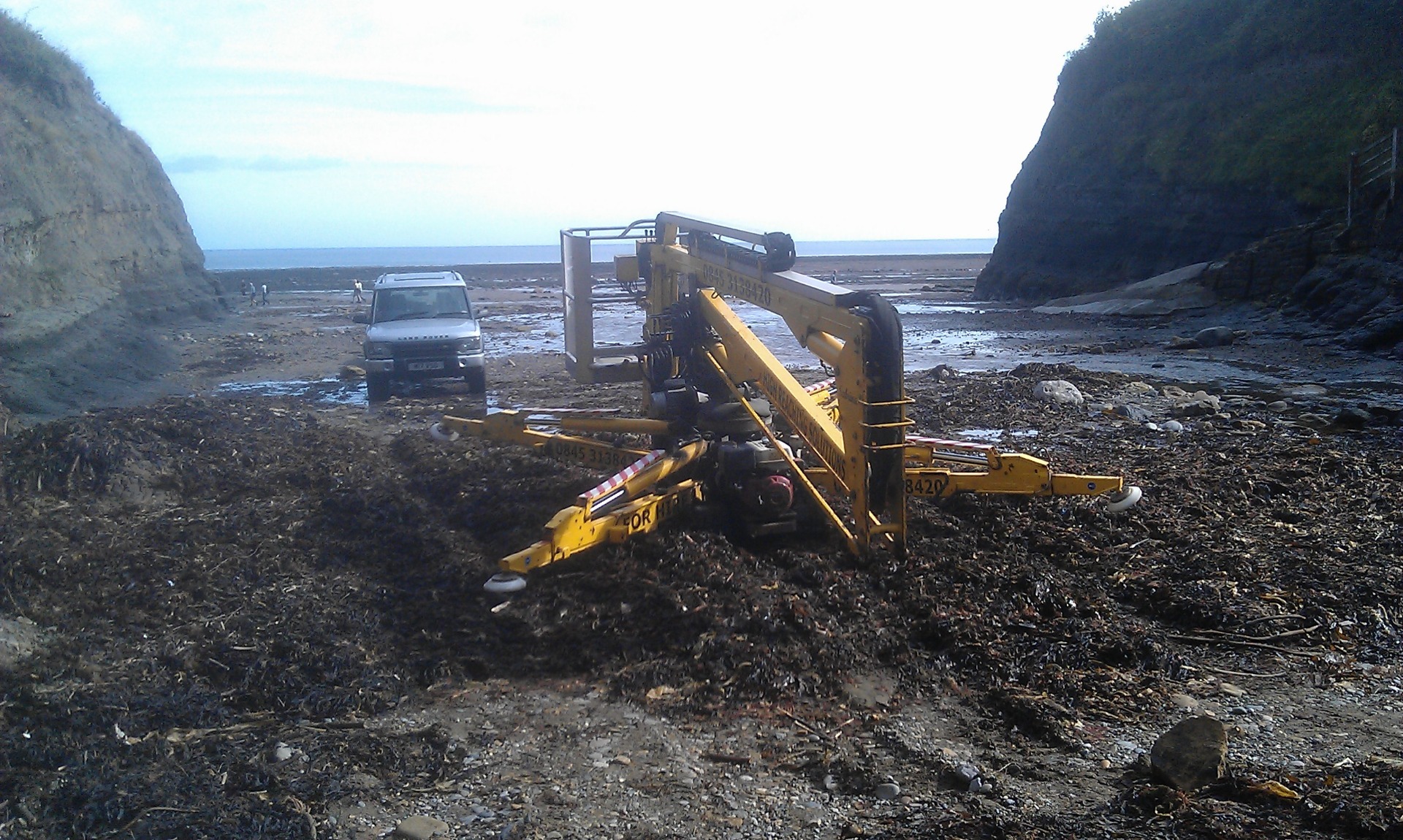 Sabrina the tracked spider cherrypicker crossing a mound of seaweed on a beach.