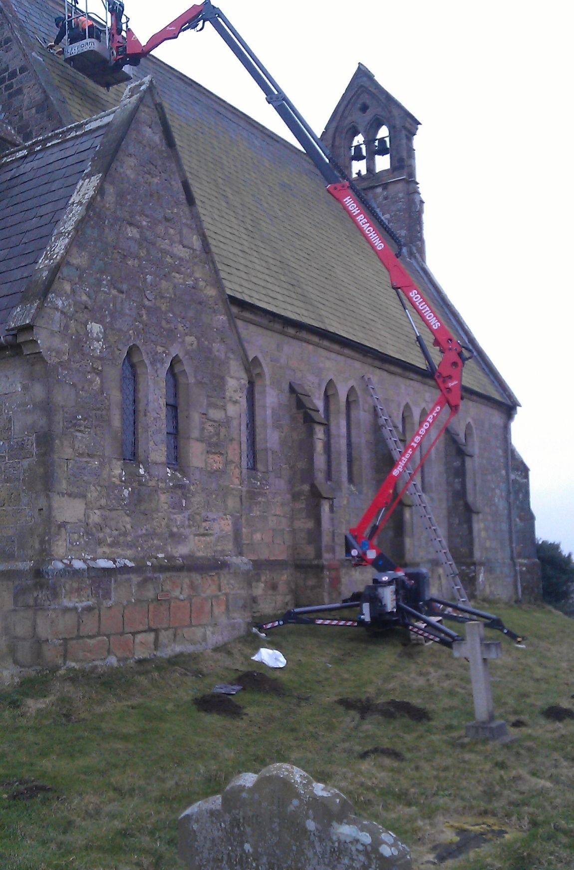 Sophie tracked spider cherrypicker working on church roof from slopped ground in churchyard.